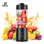 A Hacin portable electric blender with a black base and clear container, filled with strawberries and ice, surrounded by fresh fruits and orange juice splashes on a white background.