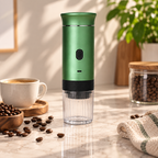 A green and black portable electric coffee grinder with a clear container, set on a marble countertop surrounded by coffee beans, a cup of coffee, and a jar of coffee beans.