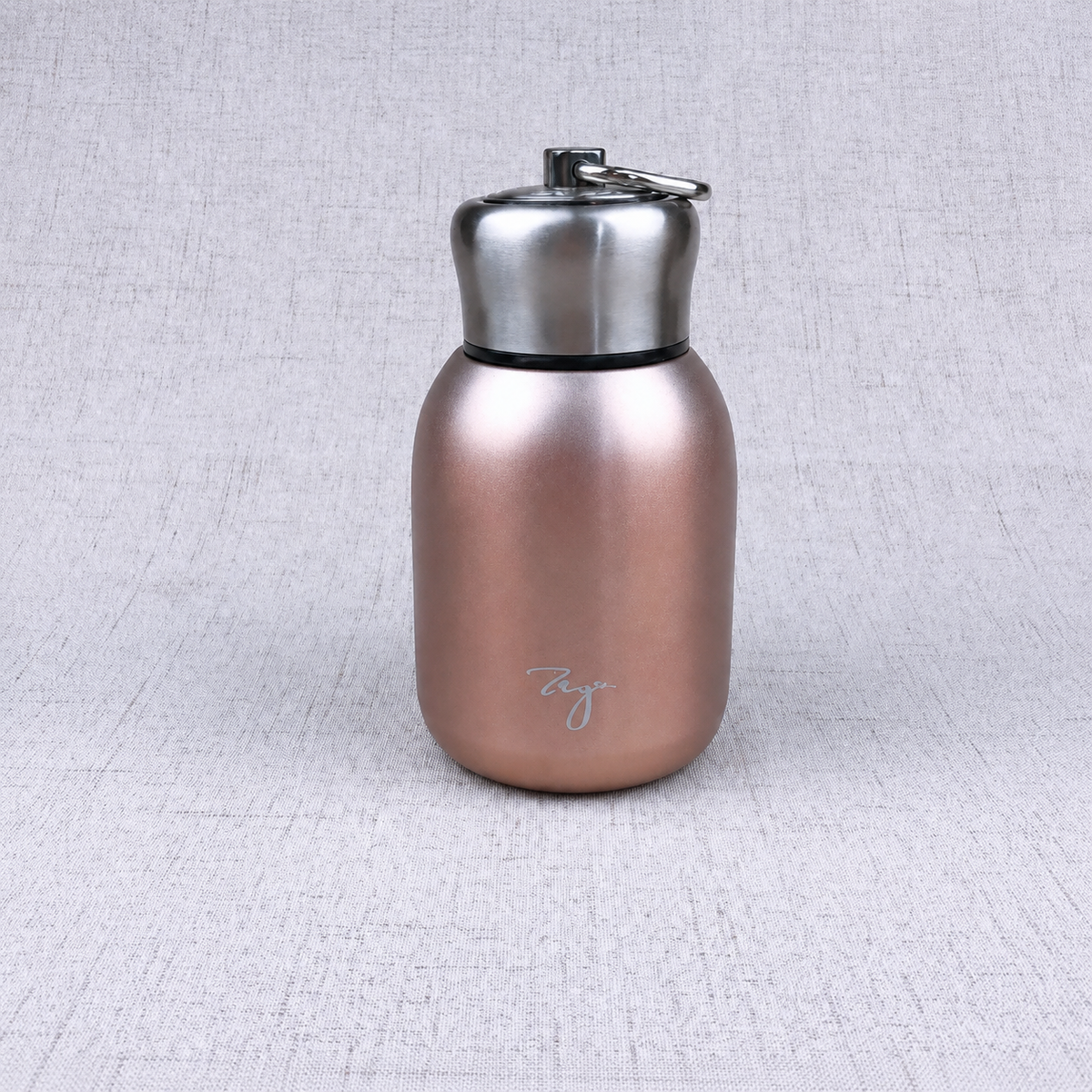 Compact insulated bottle in rose gold, with stainless-steel lid and metal carrying loop.