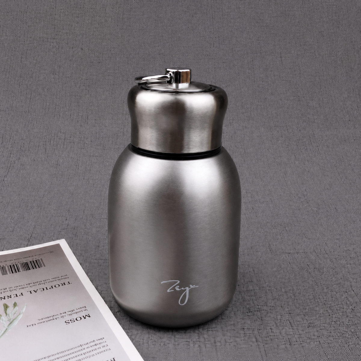 Compact insulated bottle in silver, with stainless-steel lid and metal carrying loop.