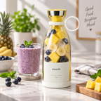 A white mini portable blender bottle filled with pineapple, blueberries, and banana, standing on a marble countertop next to a purple smoothie in a glass. The bottle has a white base and collar, a gold lid, and a white carrying loop.