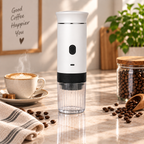 A white and black portable electric coffee grinder stands on a marble countertop in a bright kitchen setting, surrounded by coffee beans, a cup of latte art coffee, and a jar of coffee beans.
