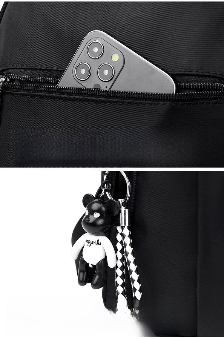 A close-up of a black backpack showing a side zip pocket with a smartphone tucked into it, and a black-and-white bear-shaped keychain with a checkered strap hanging from the main compartment.