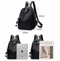 Black nylon backpack with dual shoulder straps, front zip pocket, side tassel charms, shown with dimension labels (25cm x 32cm x 11cm) and two smaller views including a tablet and magazine on a white background.